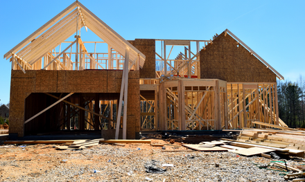 Construction of a new house; wooden frame and sheathing visible against a clear blue sky.