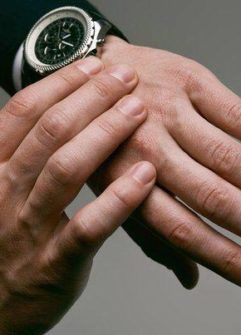 Man adjusting wristwatch, close up. Black watch face, suit sleeve visible.