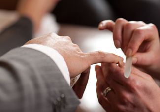 Person in a suit getting a ring placed on their finger by another person.