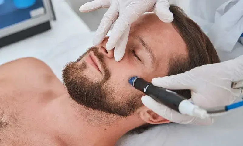 Man receiving facial treatment with gloved hands using a device.