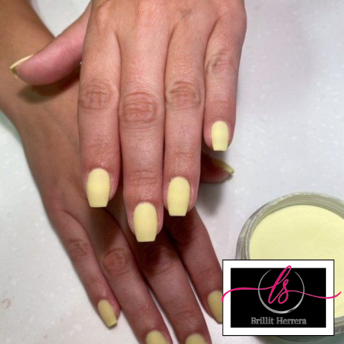 Hands with yellow square-shaped nails, next to a container of yellow nail powder.
