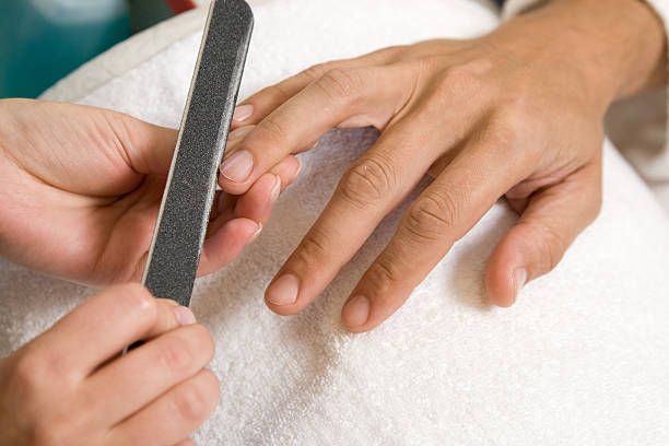 Person filing another person's fingernails with a gray nail file on a white towel.
