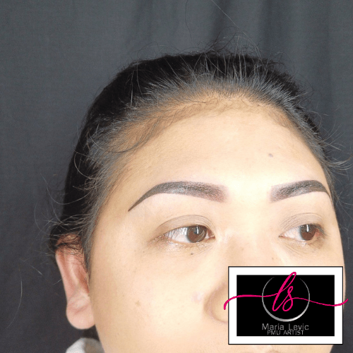 Close-up of a person's face; shows the eyes and newly tattooed eyebrows. Black background; a logo is visible in the corner.