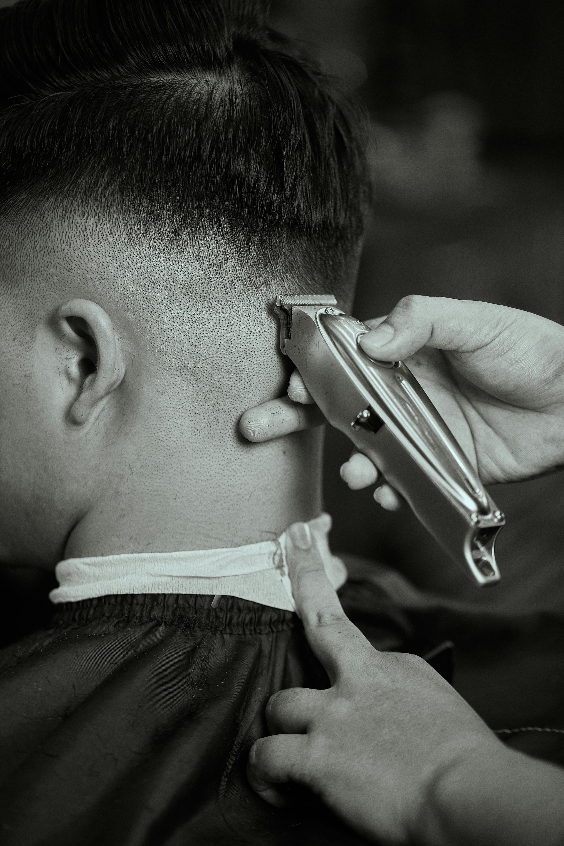 Barber giving a fade haircut, using clippers on the back of a person's head, in a salon.