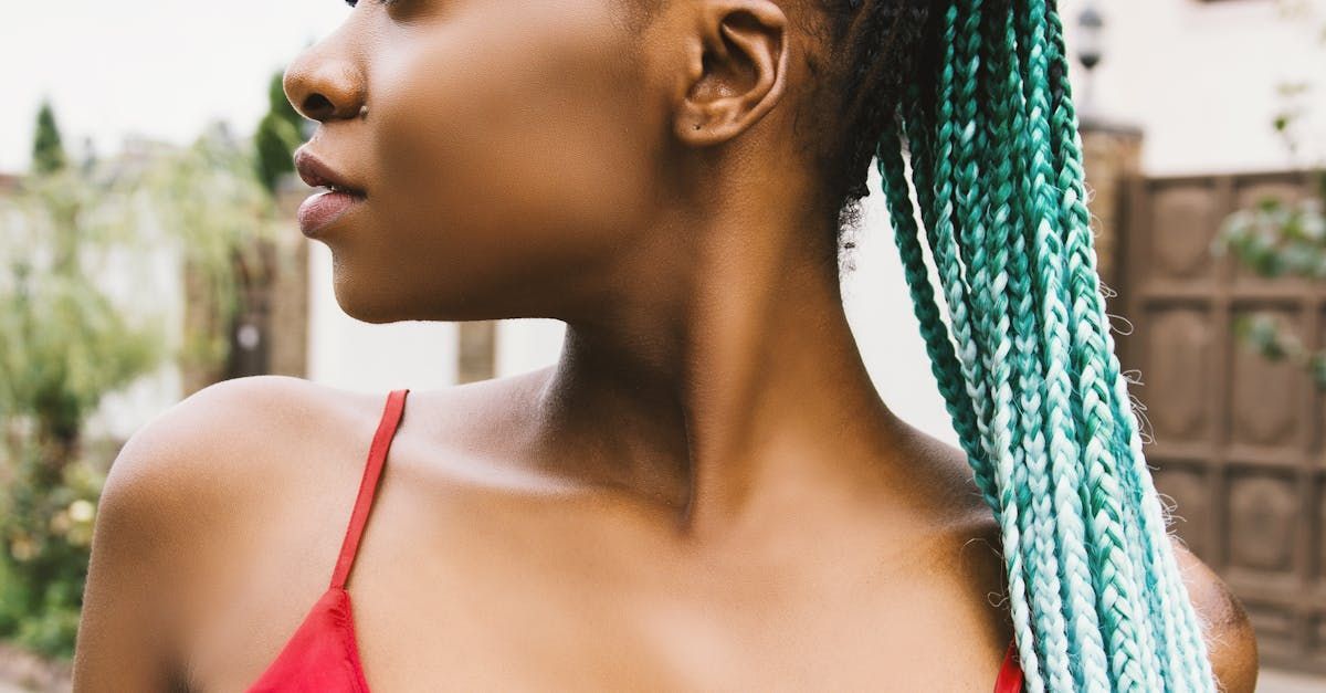Woman with teal braided hair, wearing a red top, looking to the side outdoors.