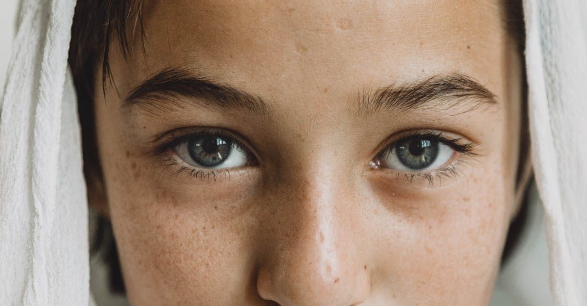 Close-up of person's face; blue eyes, dark eyebrows, and visible skin texture are prominent.