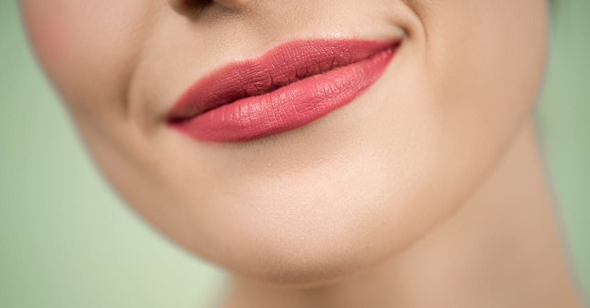 Close-up of a person's smiling mouth. Lips are painted pink, against a soft, green background.