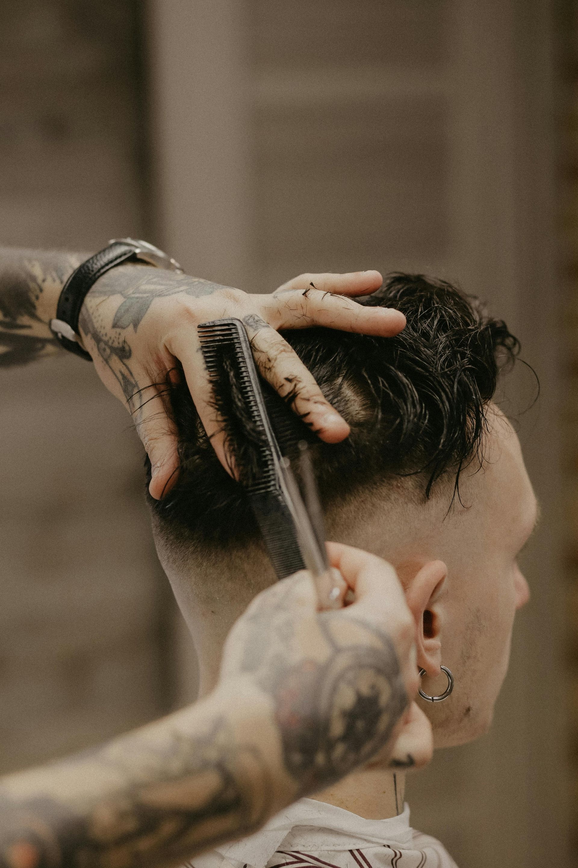 Barber cutting hair, using a comb and scissors, against a neutral background.