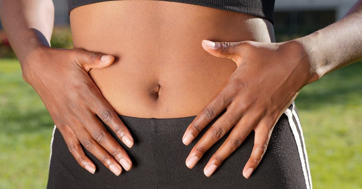 Person's hands on stomach, wearing black athletic wear, outside on a sunny day.