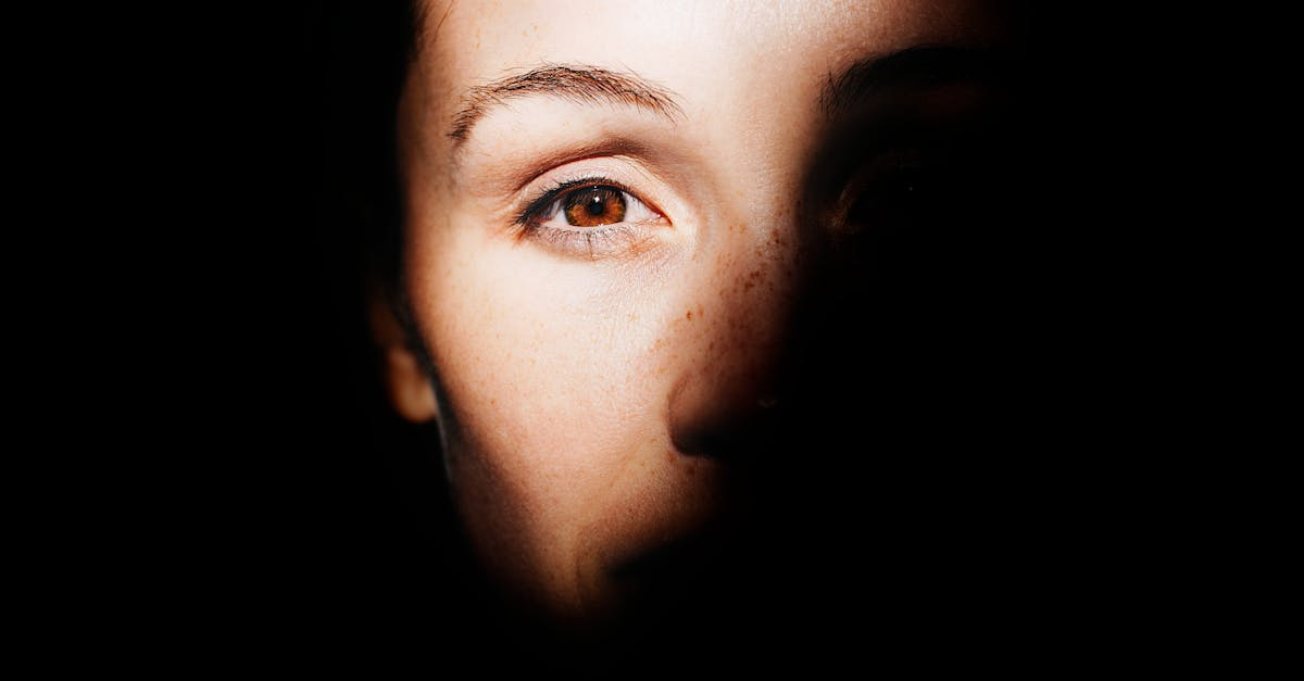 Close-up of a person's face; one eye visible with light highlighting part of the face, the rest is in shadow.