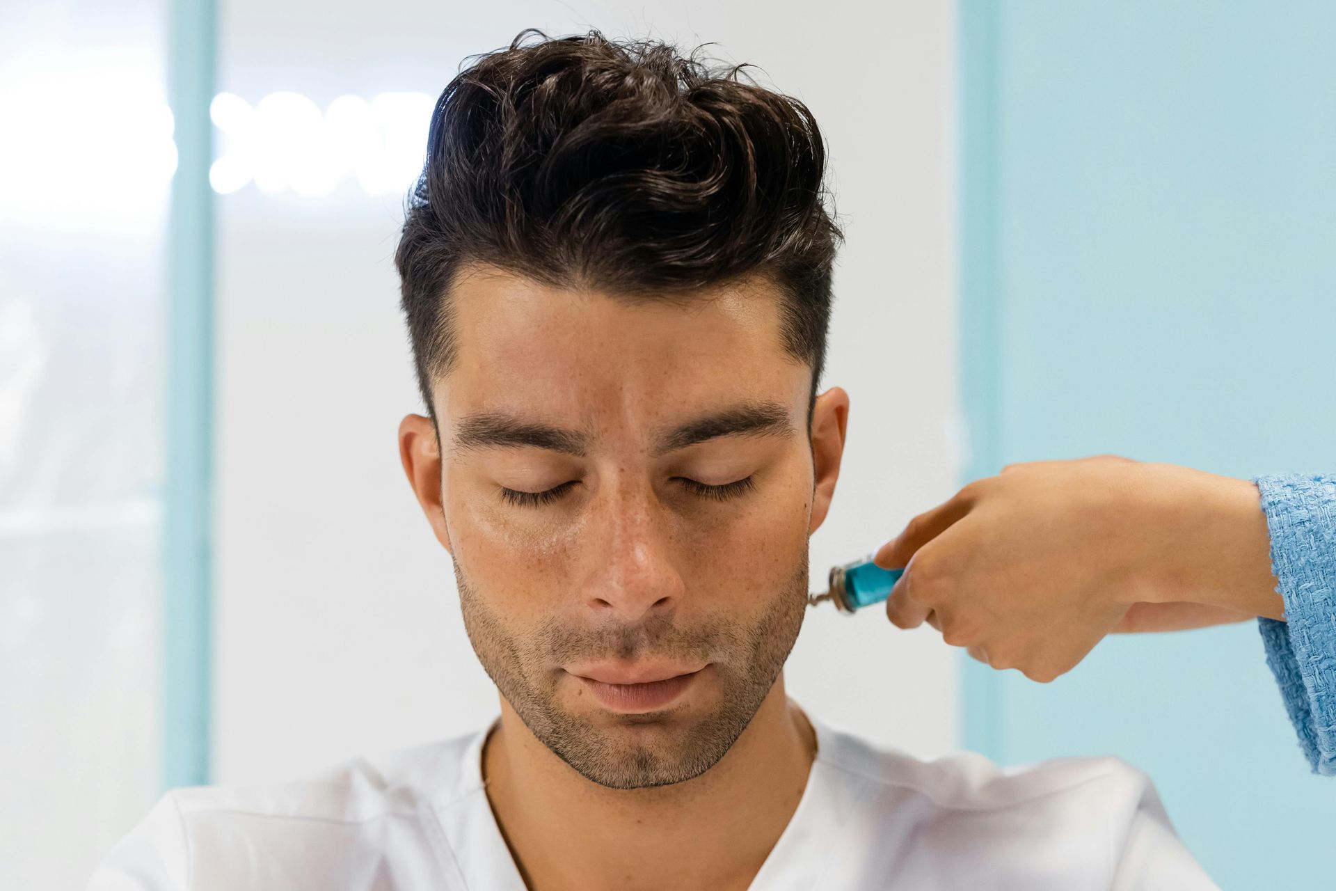 Man receiving a cosmetic treatment on his face with eyes closed, hand holding a device.