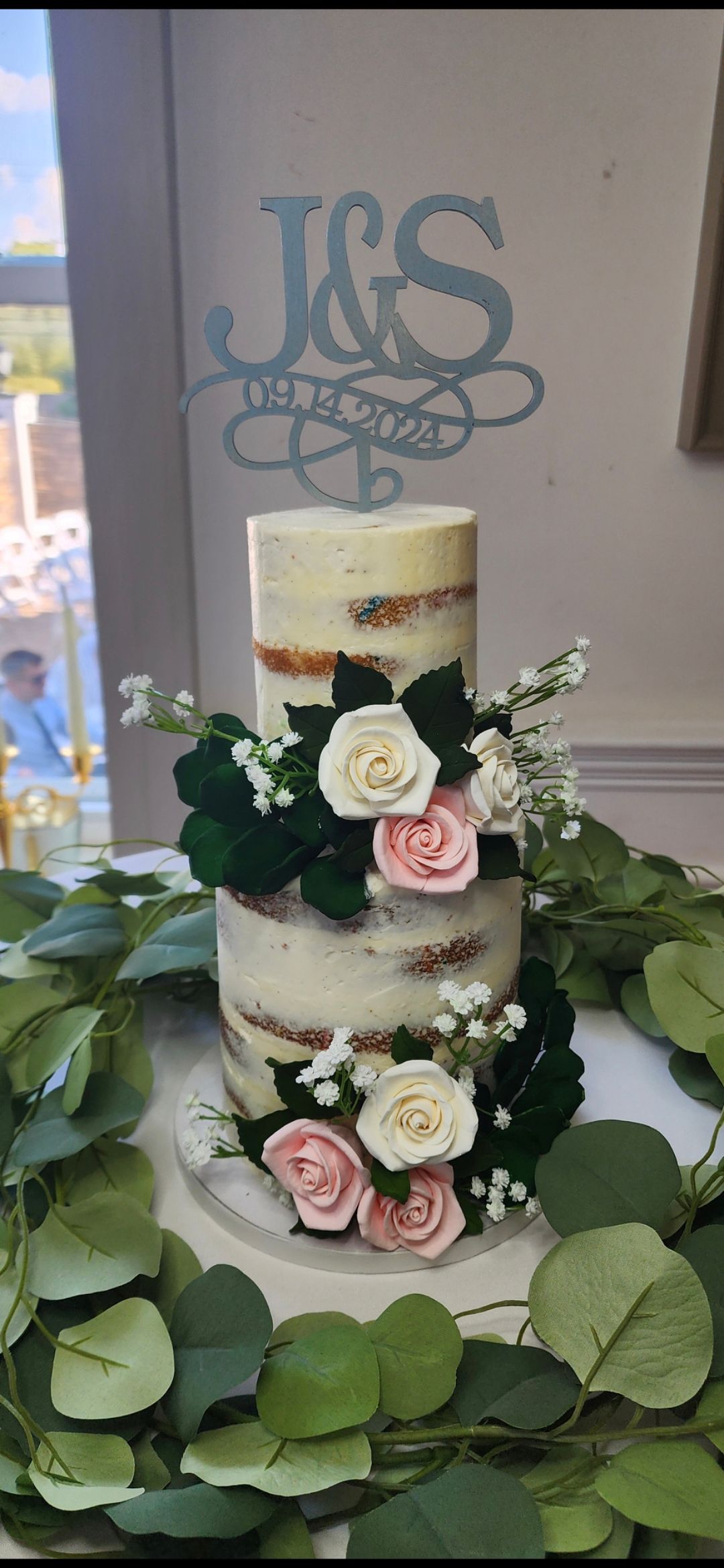 A wedding cake with flowers and leaves on it is on a table.