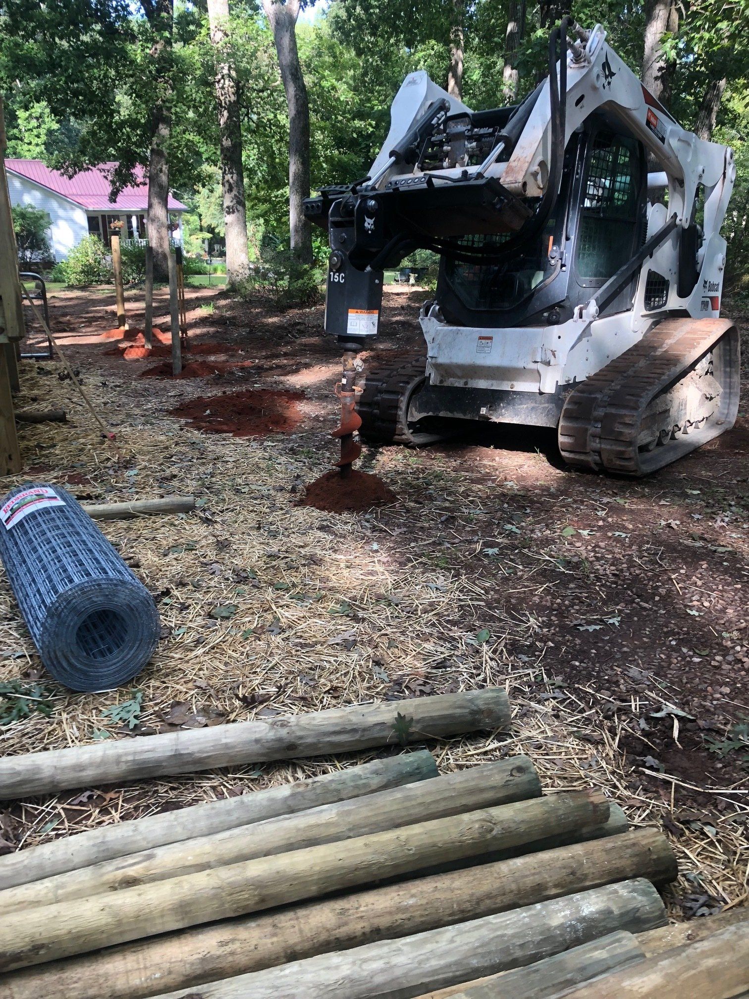 a bulldozer is digging a hole in the ground next to a pile of wooden poles .