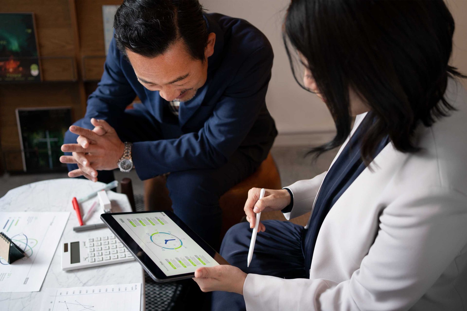 A man and a woman are sitting at a table looking at a tablet.