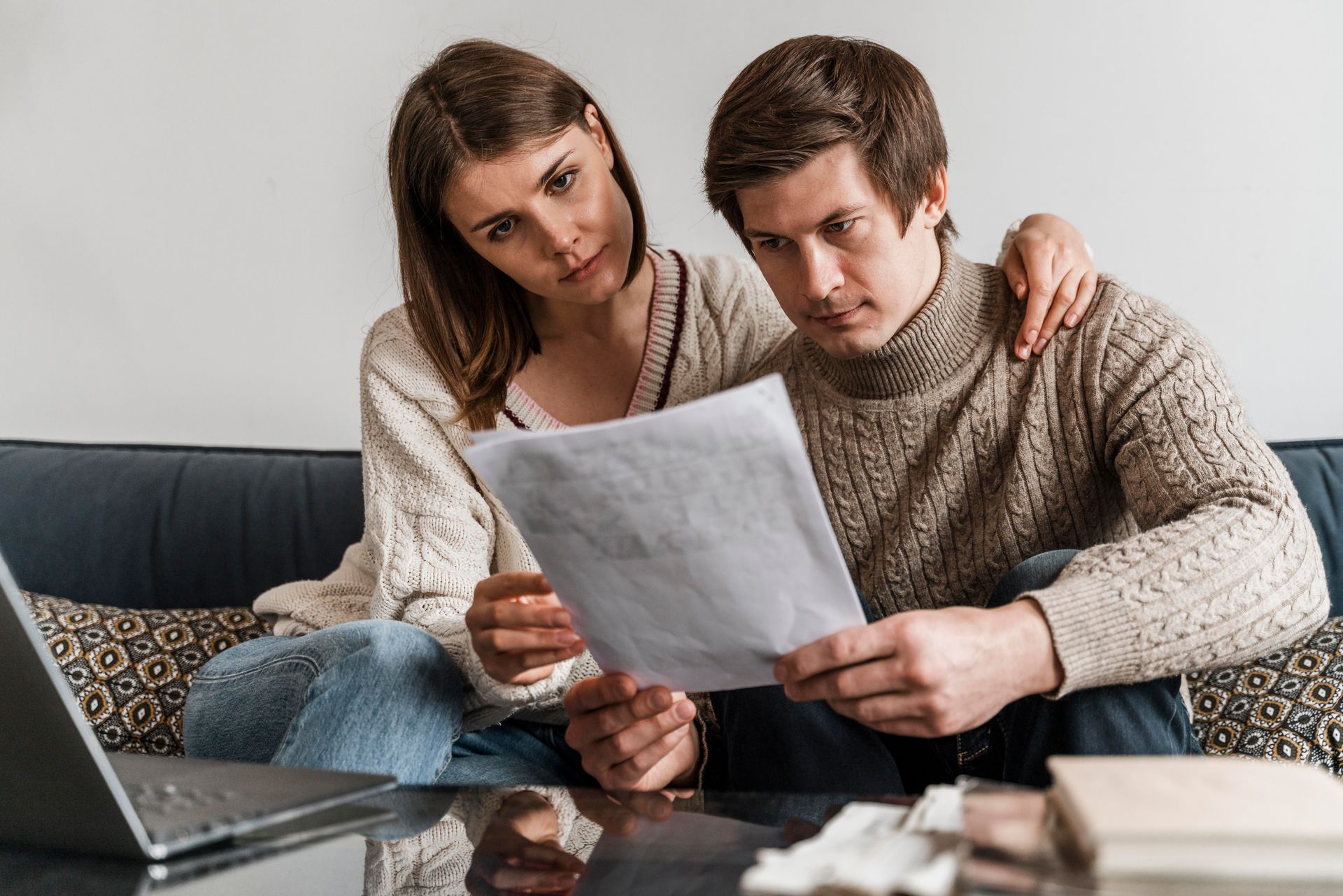 A man and a woman are sitting on a couch looking at a piece of paper.
