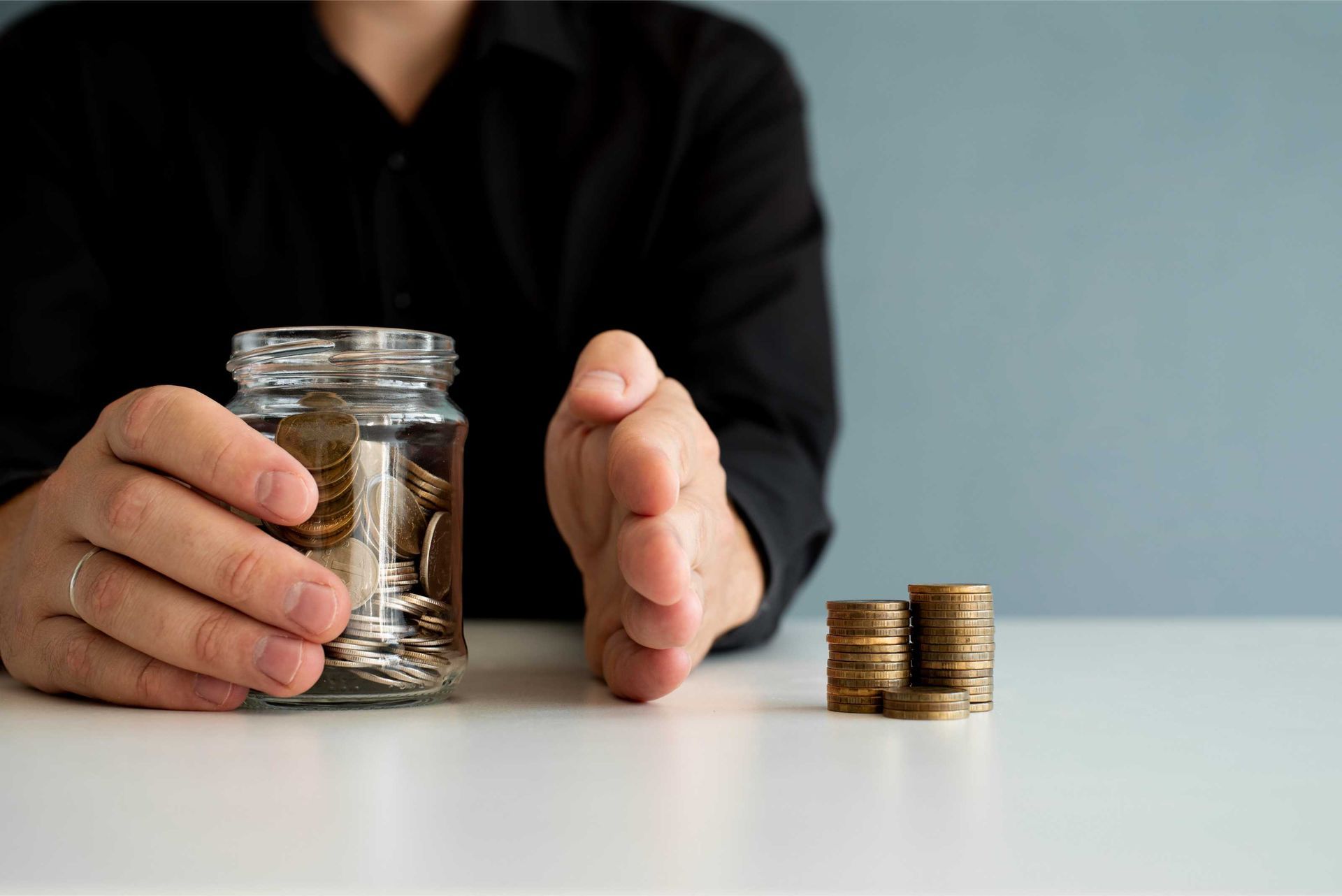 A man is holding a jar of coins and stacks of coins on a table.