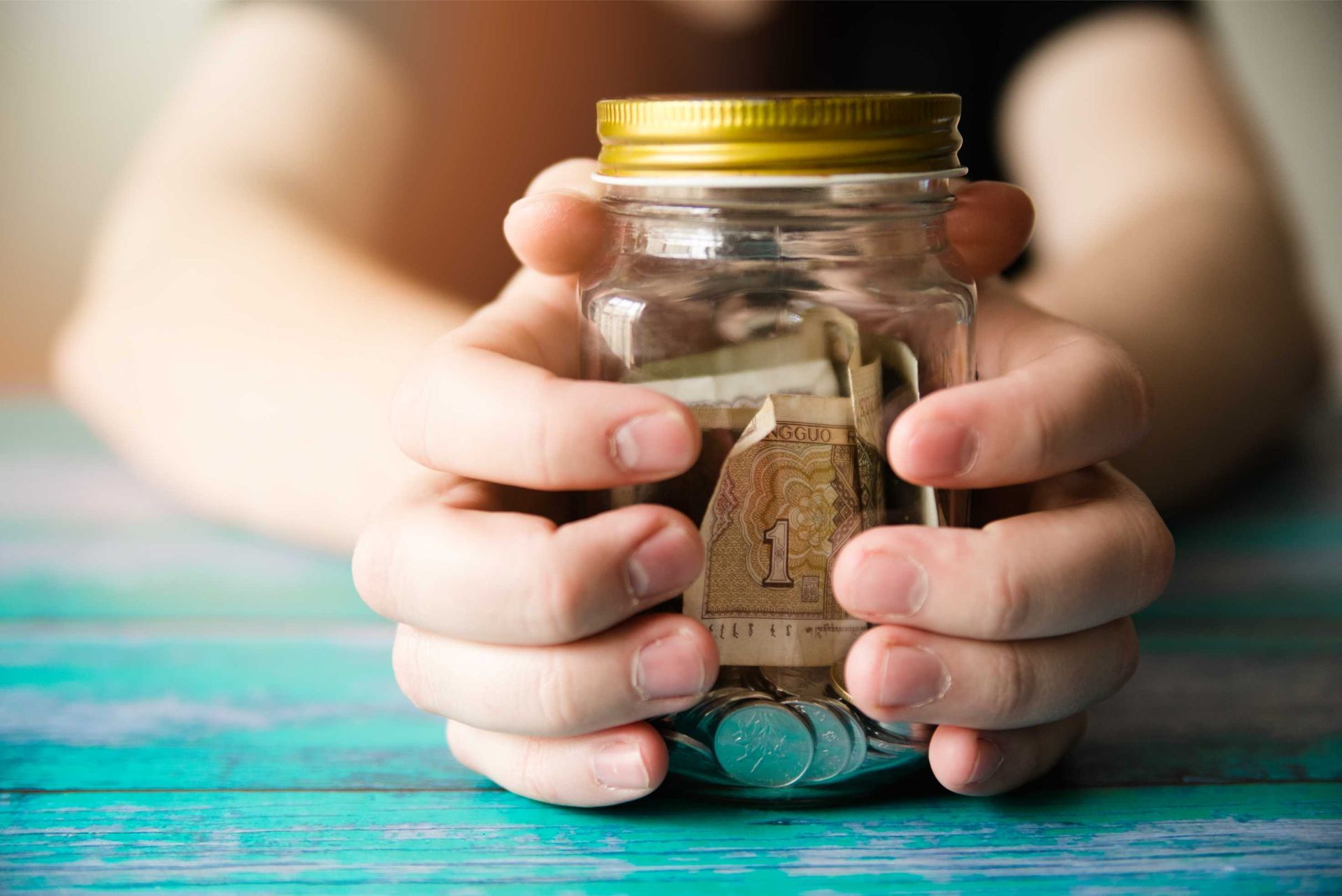 A person is holding a jar filled with money and coins.