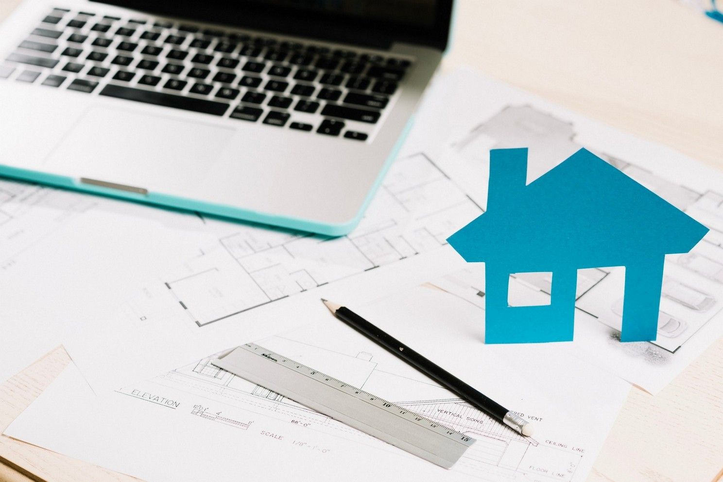 A model house is sitting on top of a table next to a laptop and a ruler.