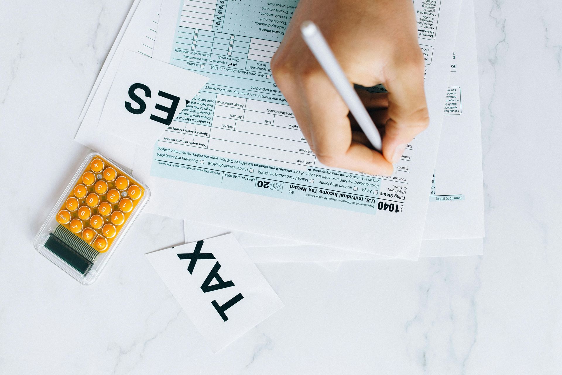 Person filling out tax forms with a calculator on a white surface.