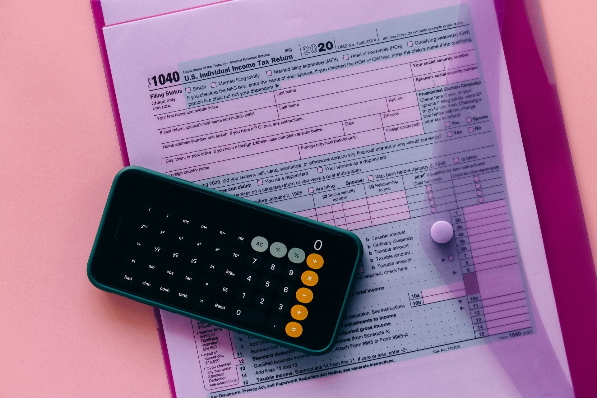 Calculator on top of a 1040 tax form in a clear file folder on a pink surface.