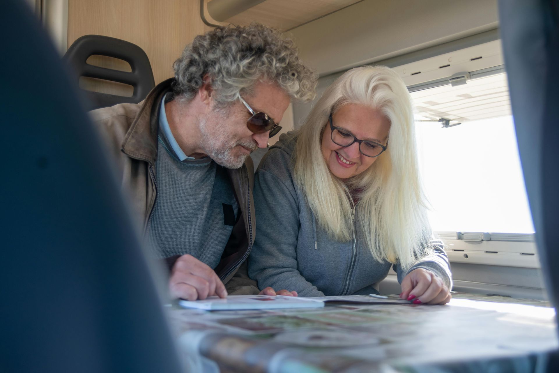Couple inside a campervan looking at a map, smiling. Sunlight streams in.