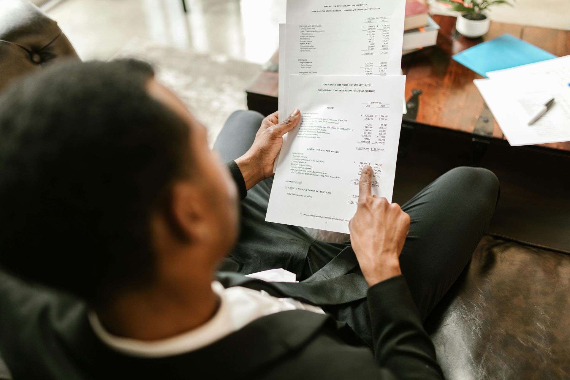 Person in a suit jacket reviews papers, pointing at the document while seated.
