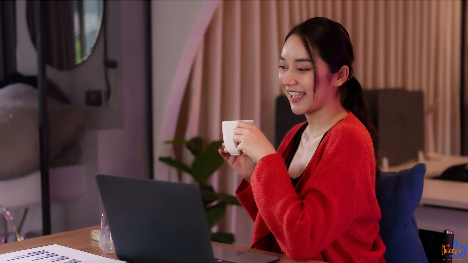 Woman writing with a pen on a paper, at a counter. She wears a brown jacket with a chain strap.