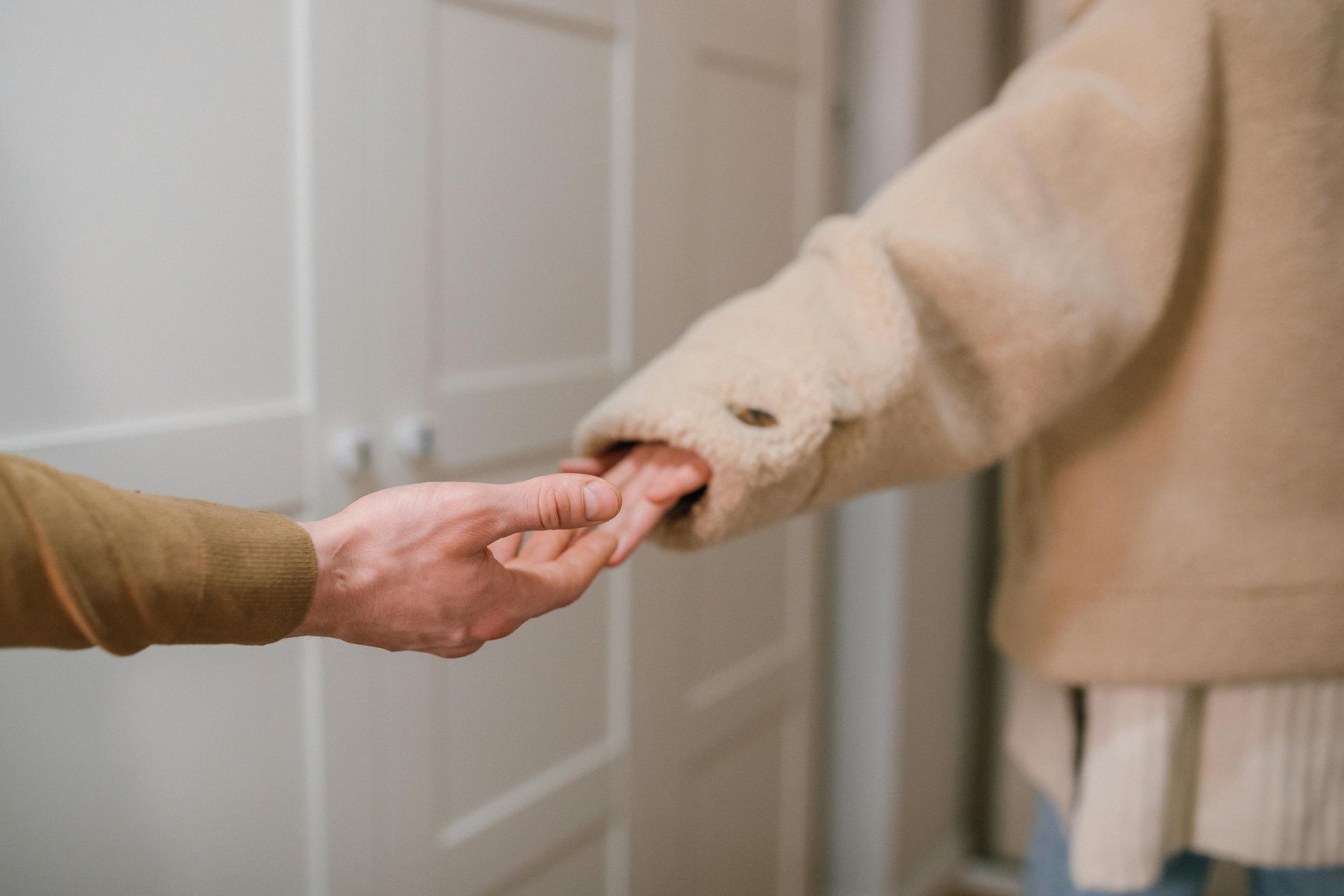 Two people holding hands, one in a beige coat, near a white wardrobe.
