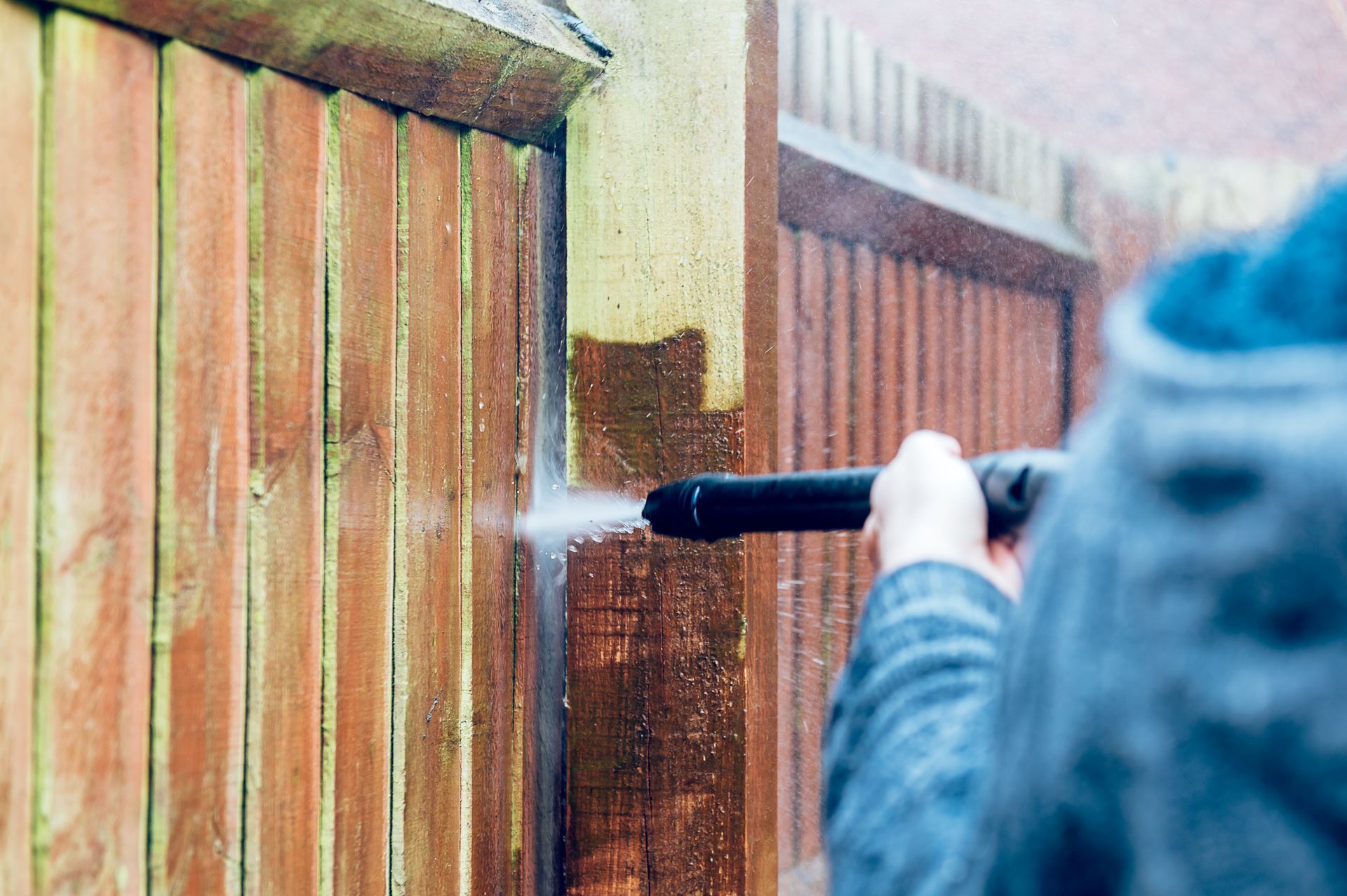 A person is using a high pressure washer to clean a wooden fence.
