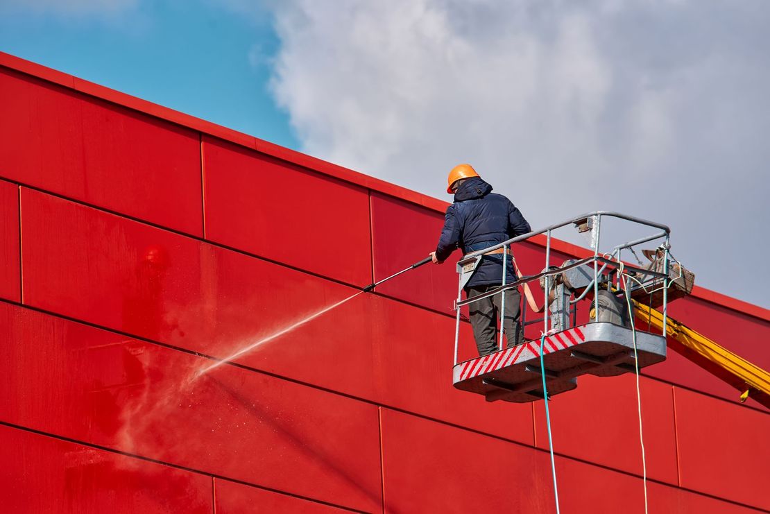 A man is cleaning a red building with a high pressure washer.