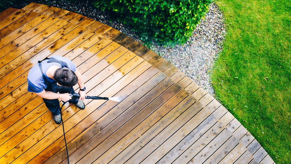 A person is using a high pressure washer to clean the deck of a house.