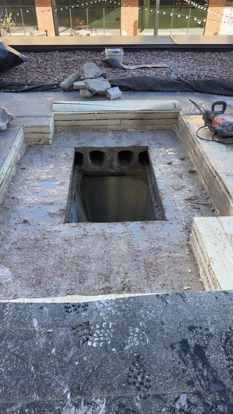 Construction site: open square hole in a concrete surface, surrounded by wooden beams and construction materials.