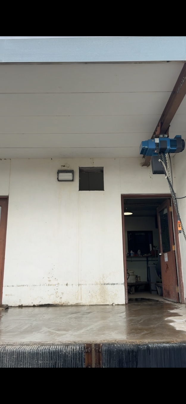 Exterior of a loading dock, with a blue hoist and a door.