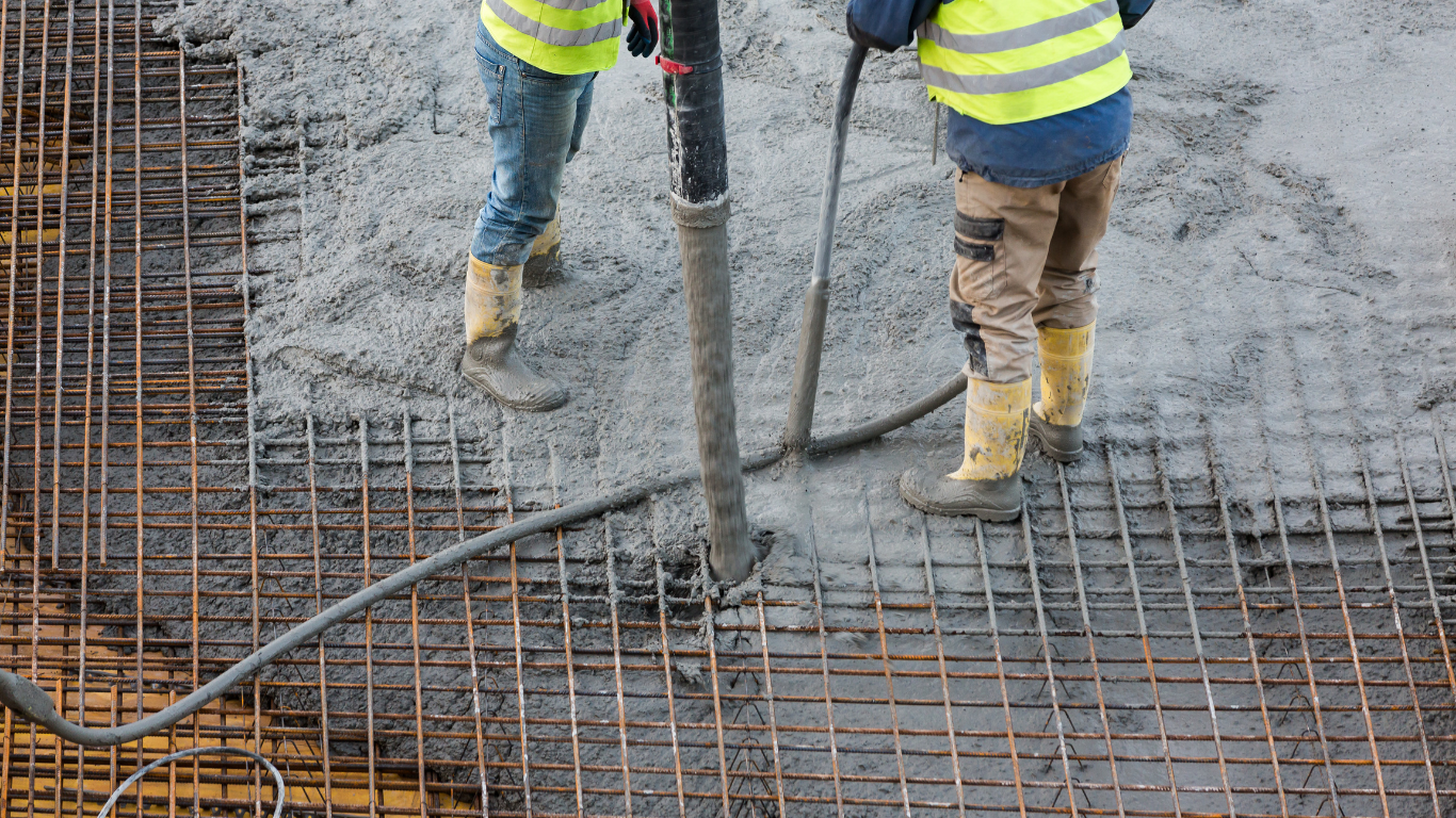 Construction workers pouring concrete on rebar foundation, wearing safety vests and boots.