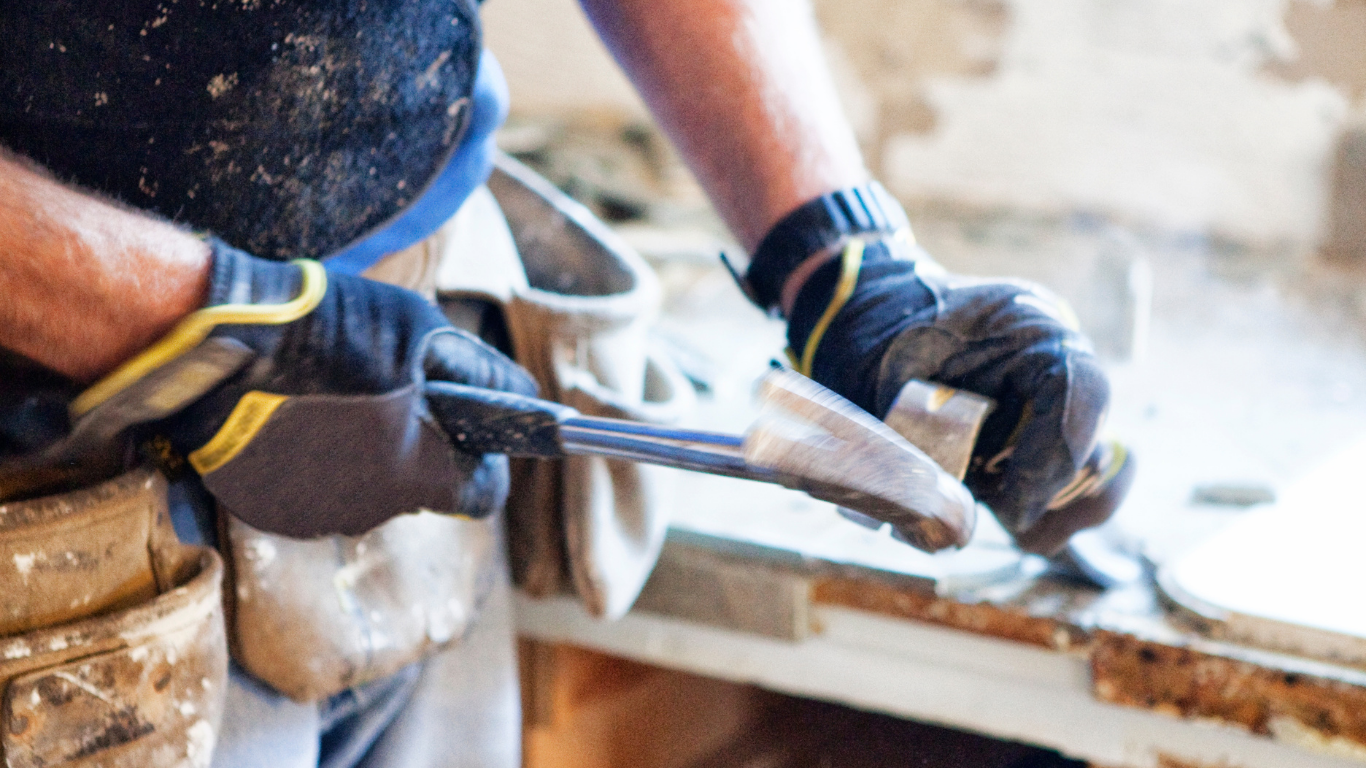 Person wearing work gloves, using a pry bar to remove debris during a renovation.