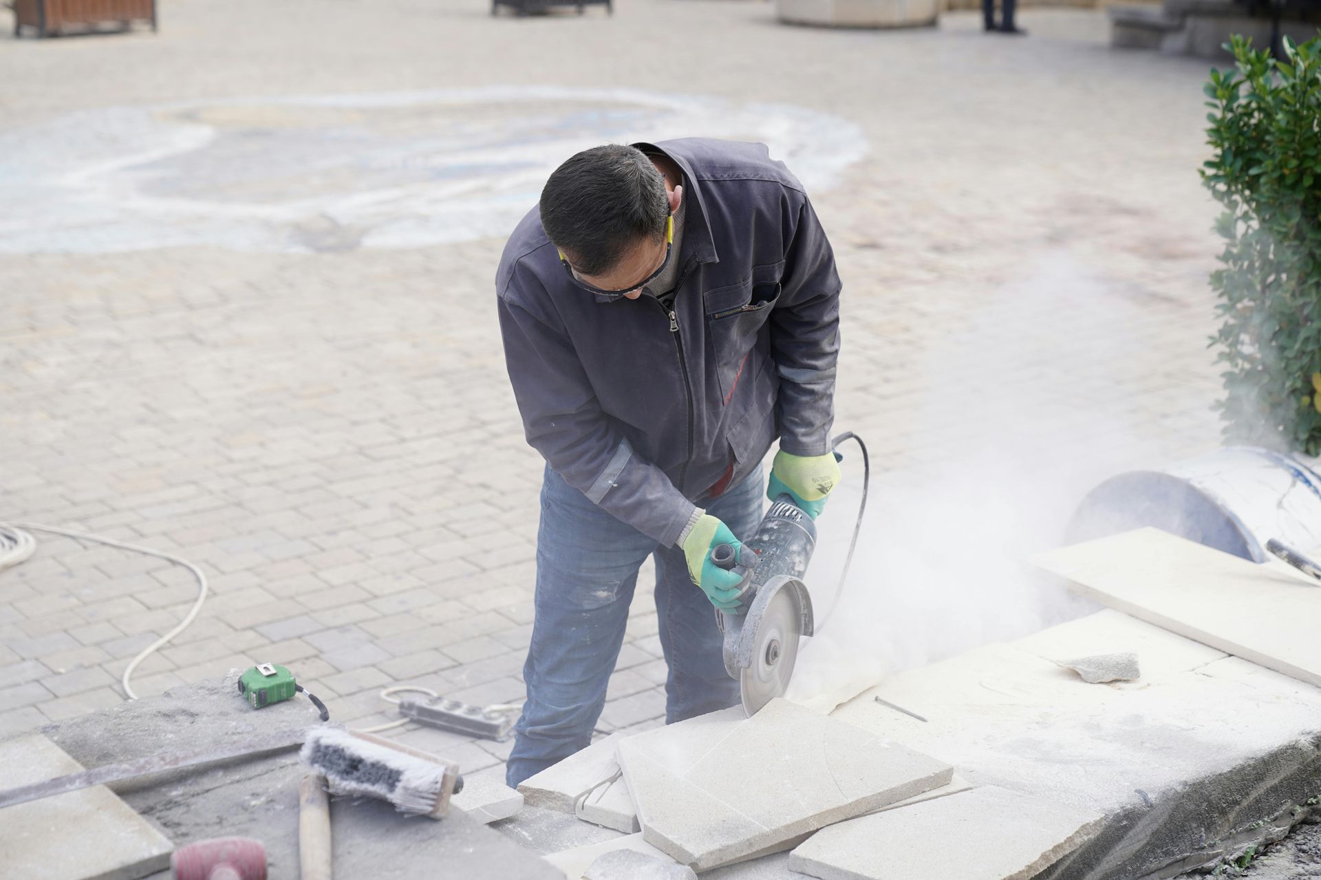 Man cutting stone with a power saw outdoors, creating dust.