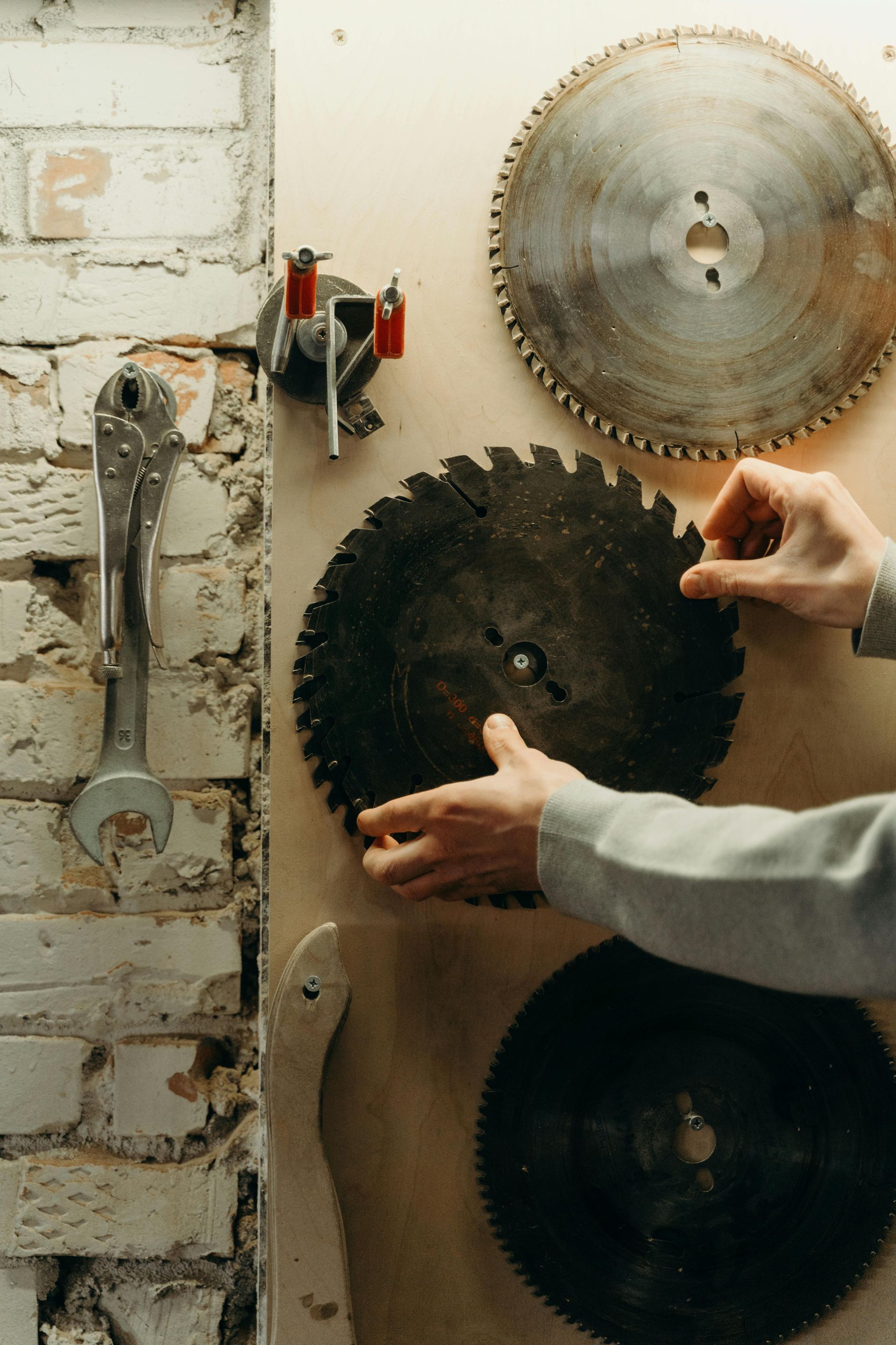 Person placing a circular saw blade on a wall with other blades and tools.