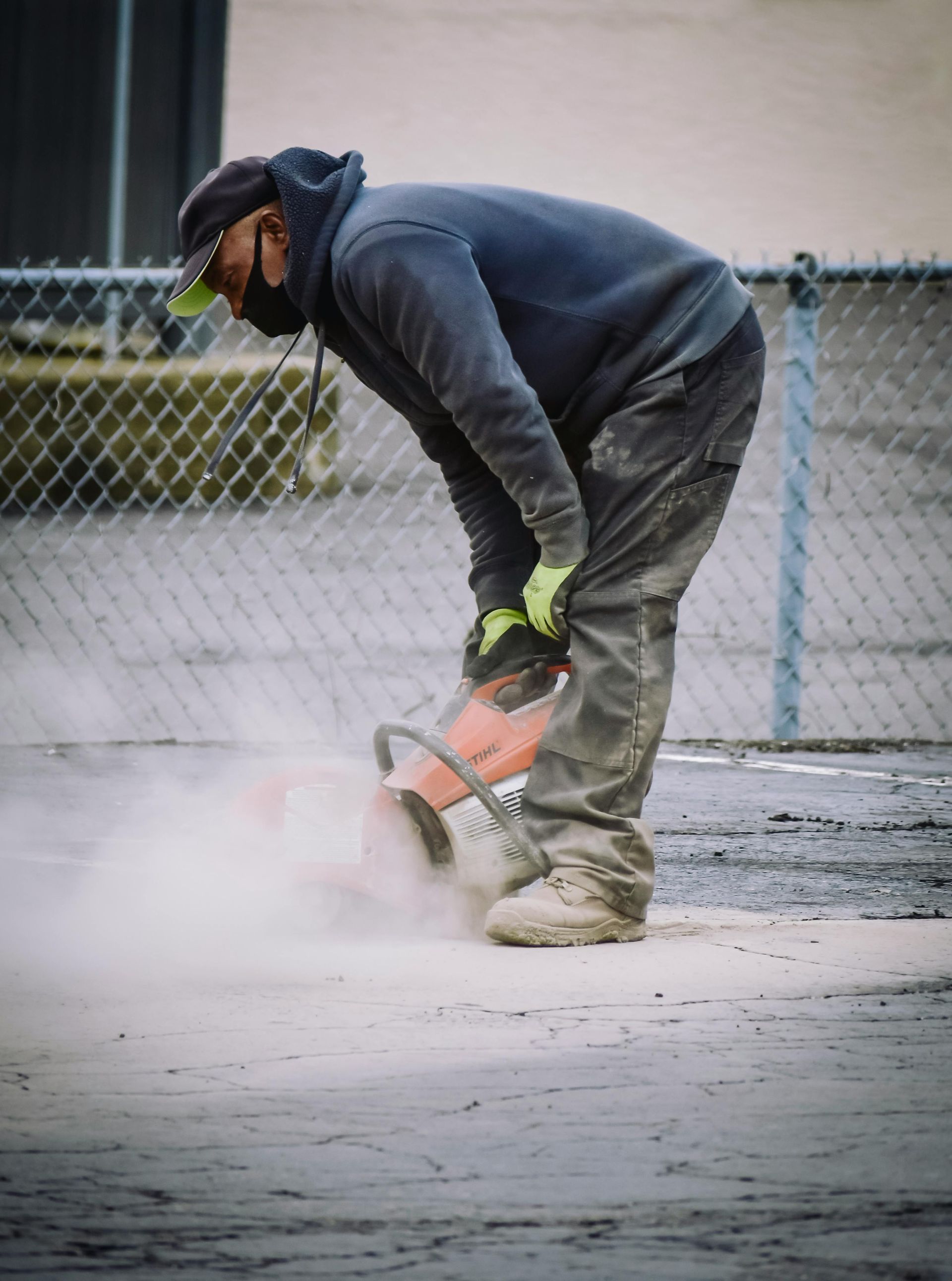 Person in work clothes cutting concrete with a power saw, creating dust.