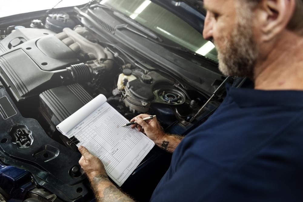A Man Is Looking Under The Hood Of A Car While Writing On A Notepad — Ballina Rego & Mechanical Centre In Ballina, NSW