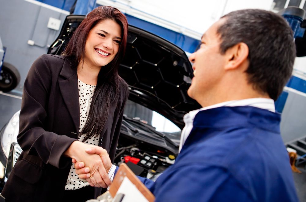 A Woman Is Shaking Hands With A Mechanic In A Garage — Ballina Rego & Mechanical Centre In Ballina, NSW