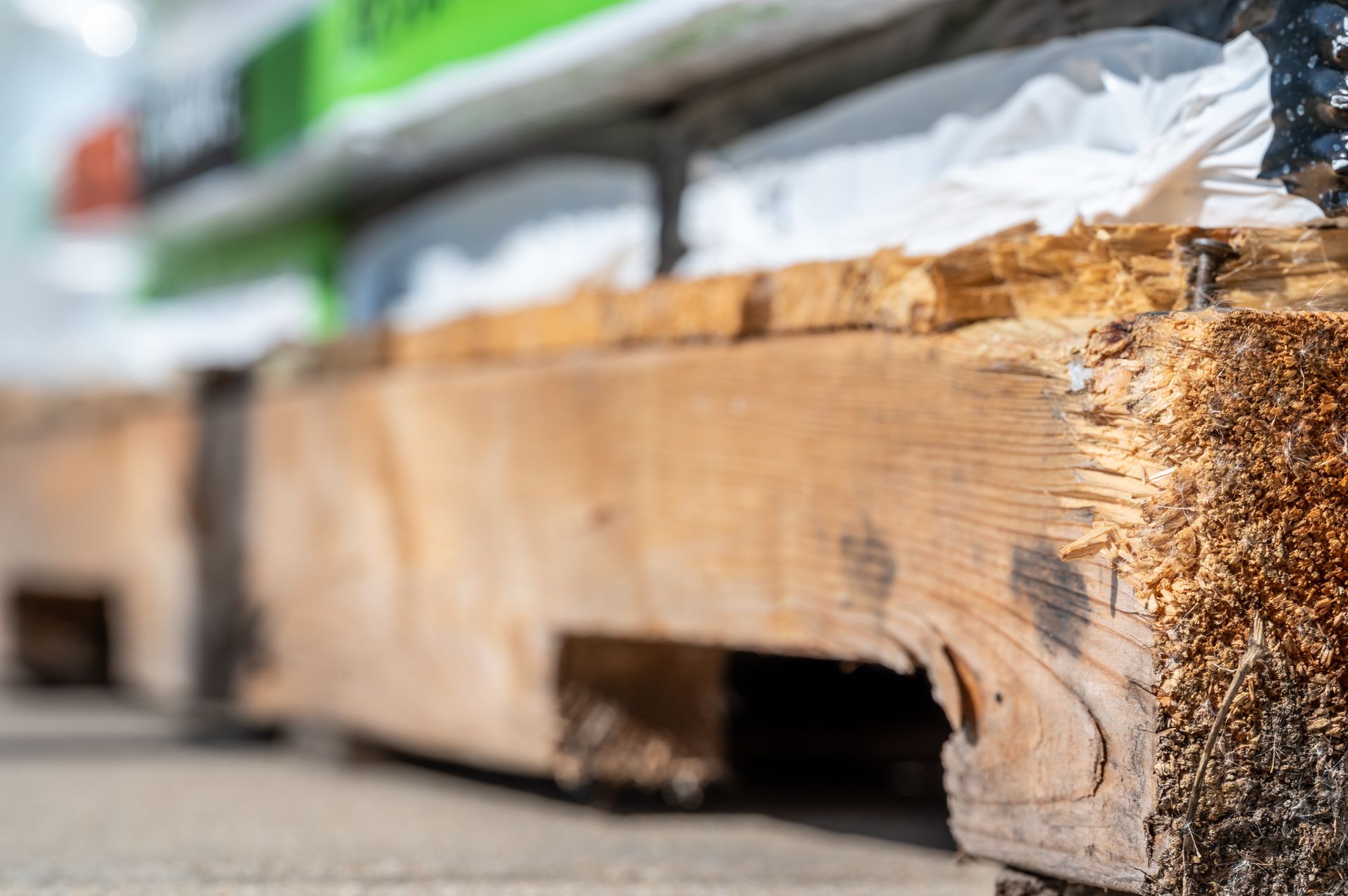 Close-up of a wooden shipping pallet resting on a concrete floor with a blurred green object in the background.