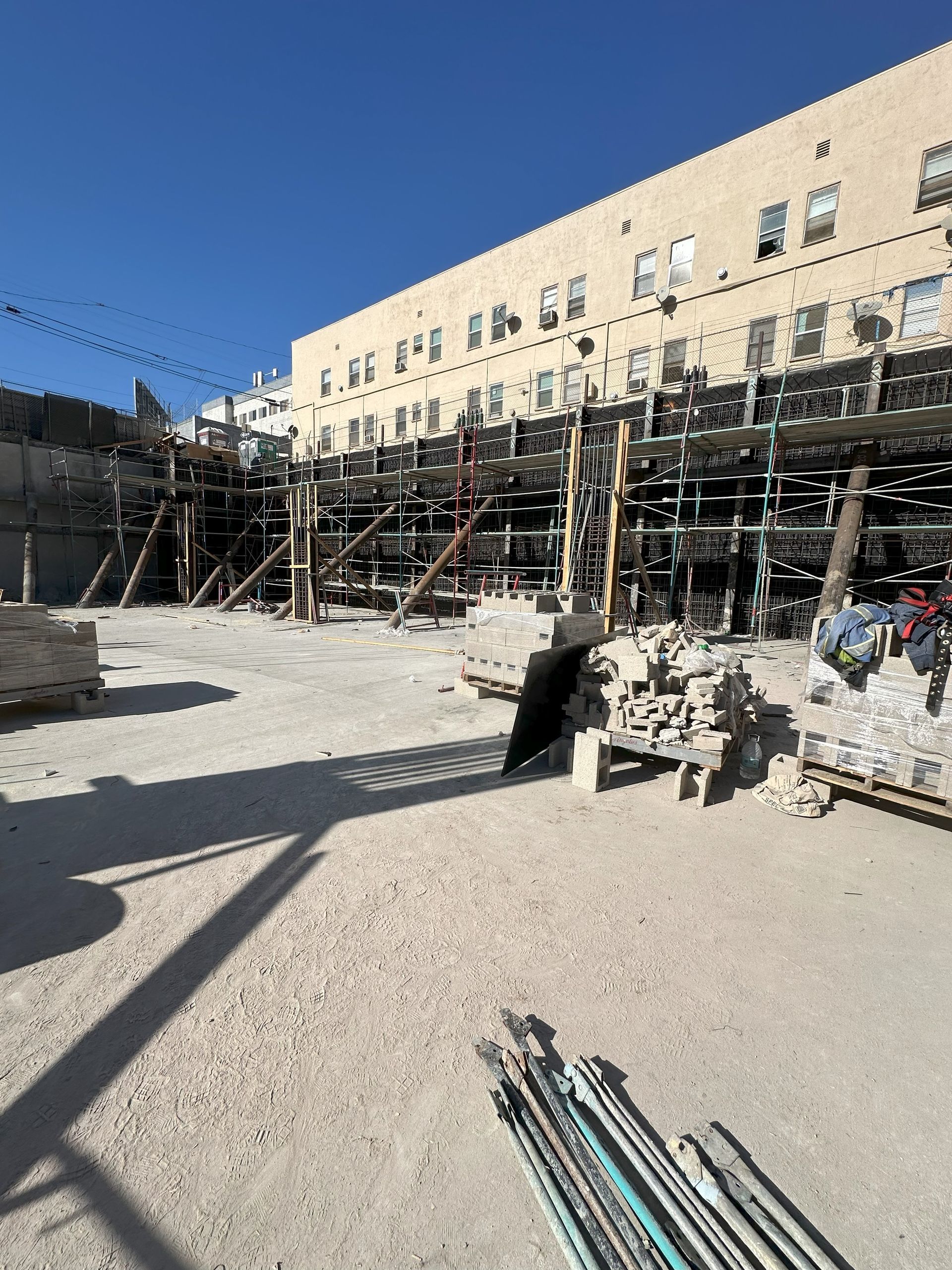 Construction site with wooden supports against a beige building. Debris and tools are scattered on a dusty ground.