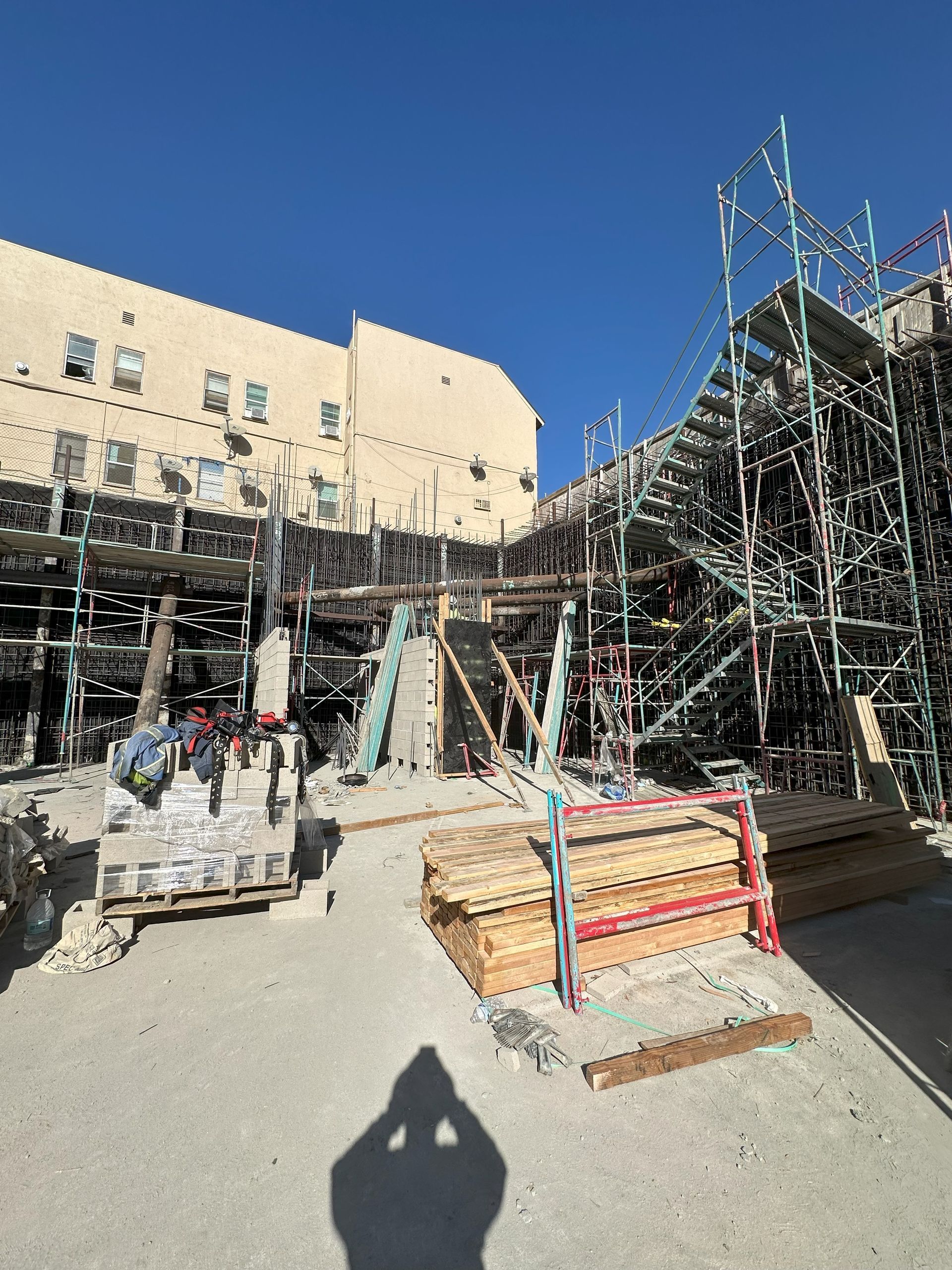 Construction site with scaffolding and materials; sunny day, shadow of person.