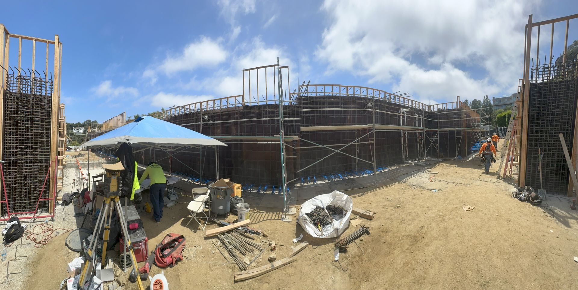 Construction site with wooden forms, workers, and blue sky.