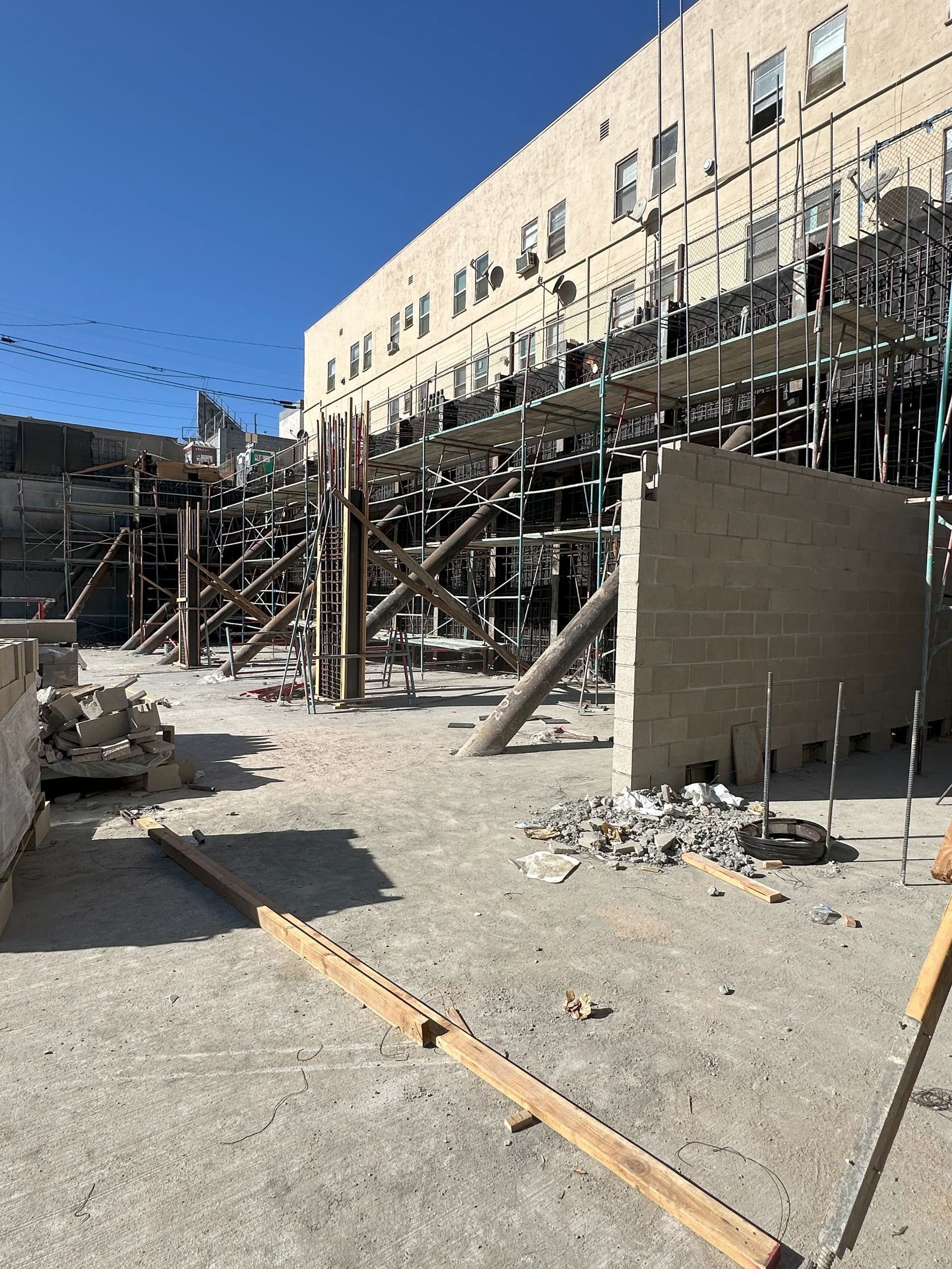 Construction site with scaffolding and building. Debris and dirt ground. Blue sky.