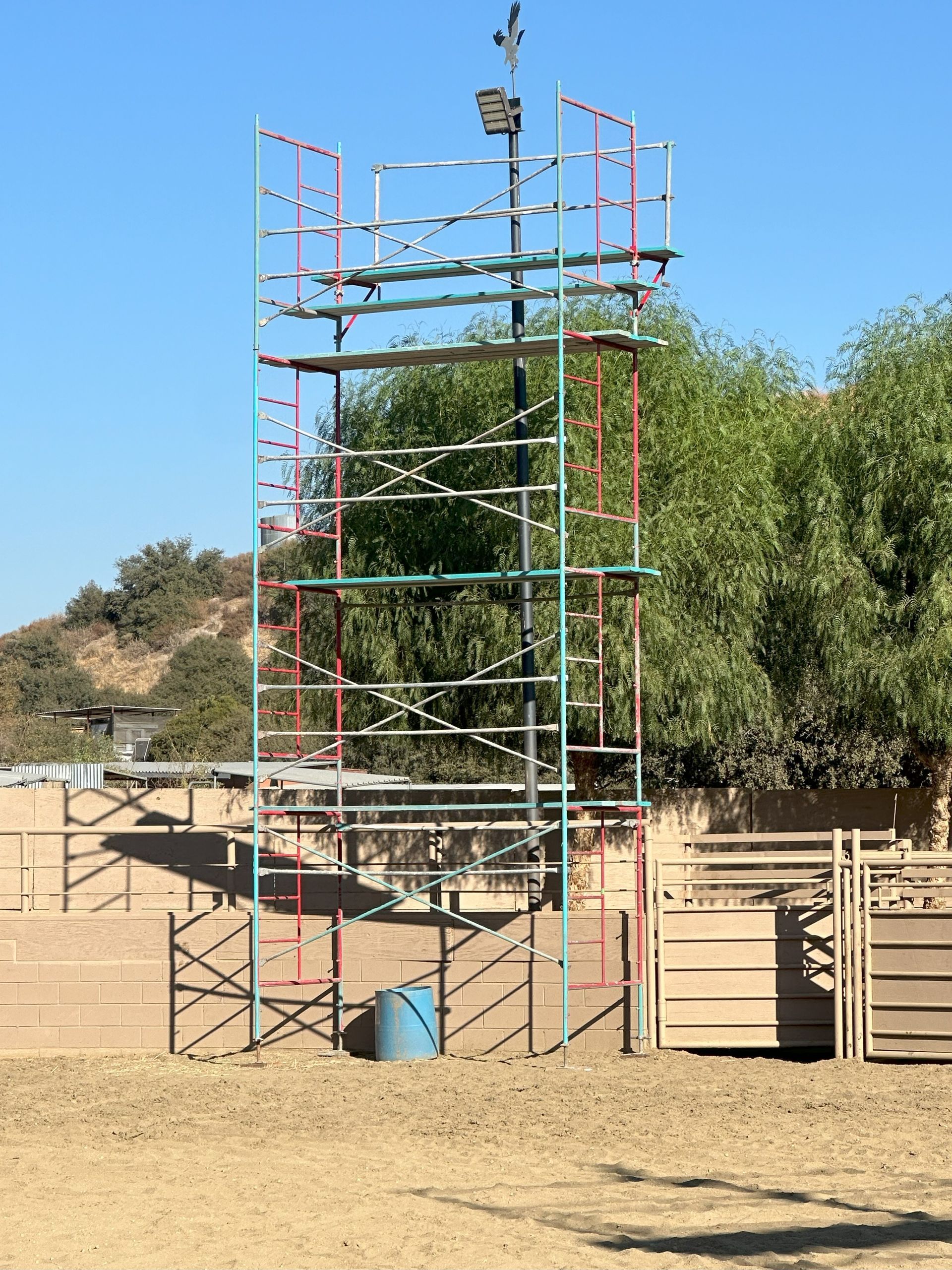 A tall metal tower with scaffolding levels, painted red, green, and blue, sits outdoors in a sandy area.