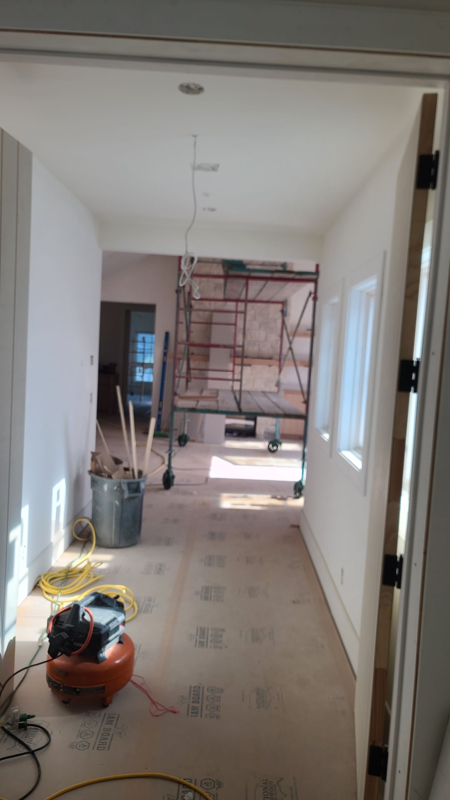 Hallway under construction, unfinished walls, scaffolding, equipment, tools, sunlight.