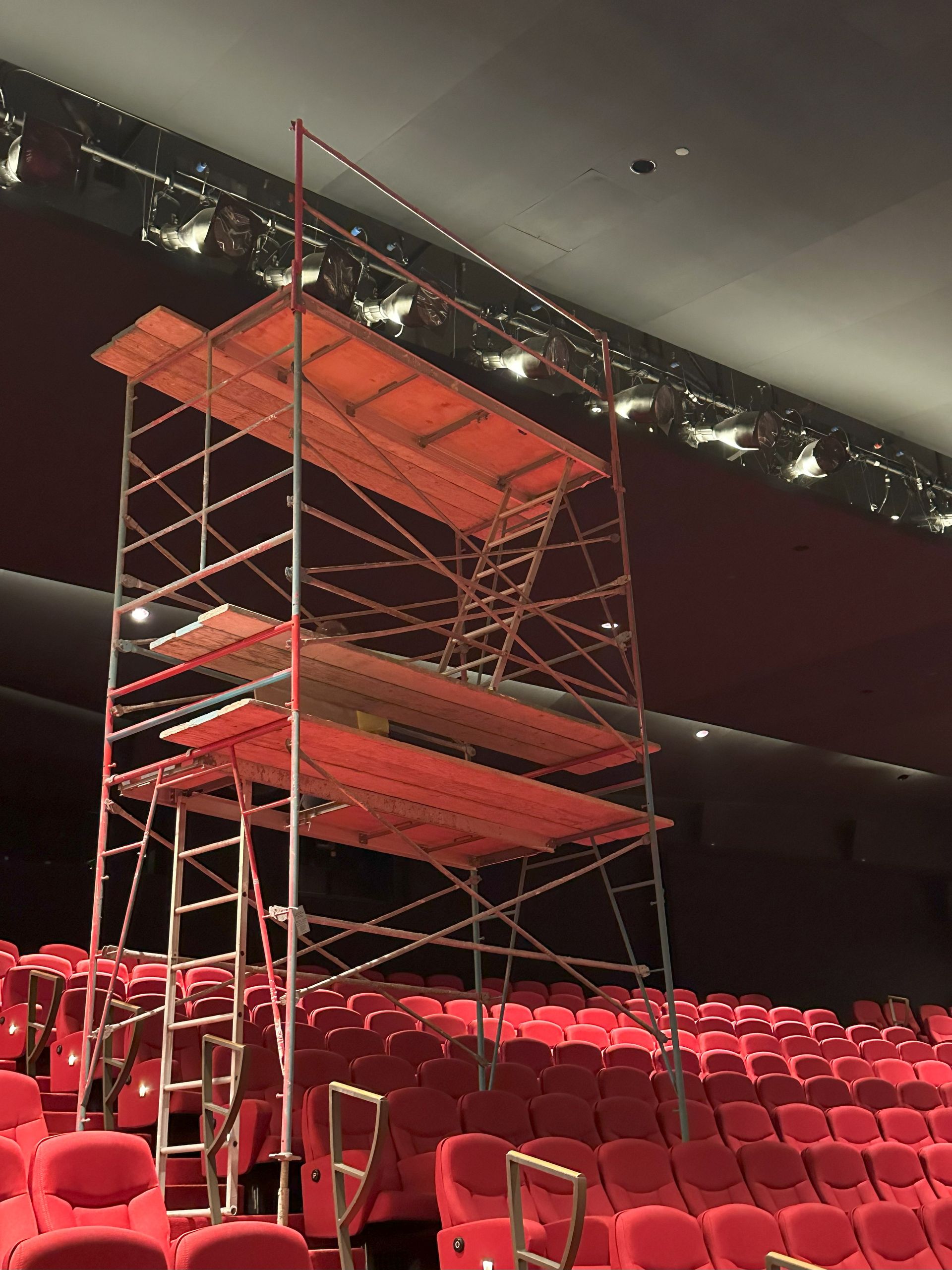 Scaffolding erected in a theater with red seating; the scaffolding is for maintenance or construction.