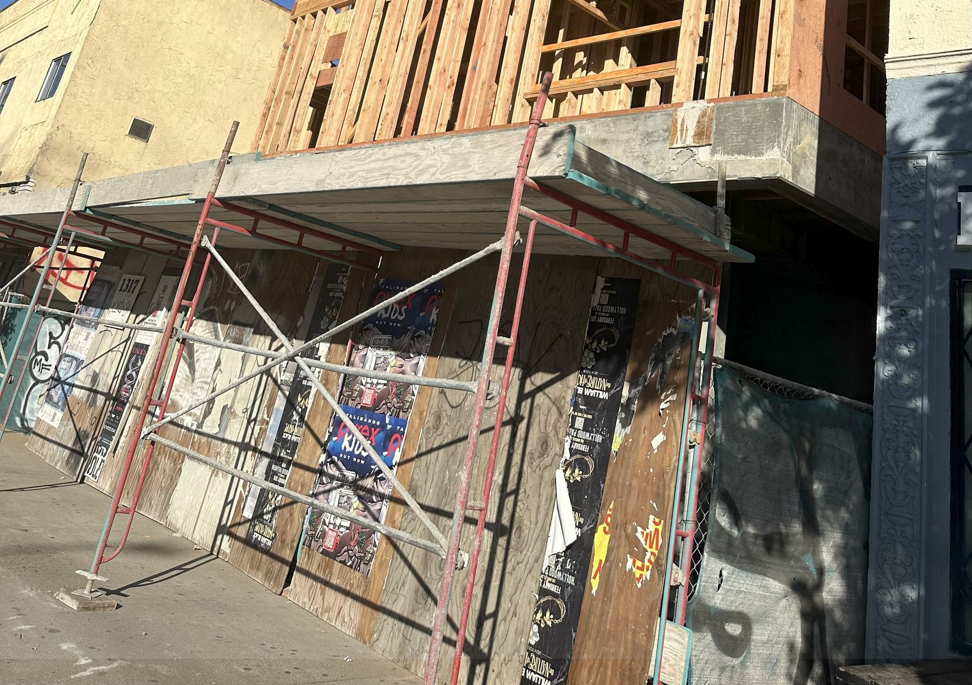 Scaffolding supports a concrete structure attached to a building under construction, with a boarded-up wall below.