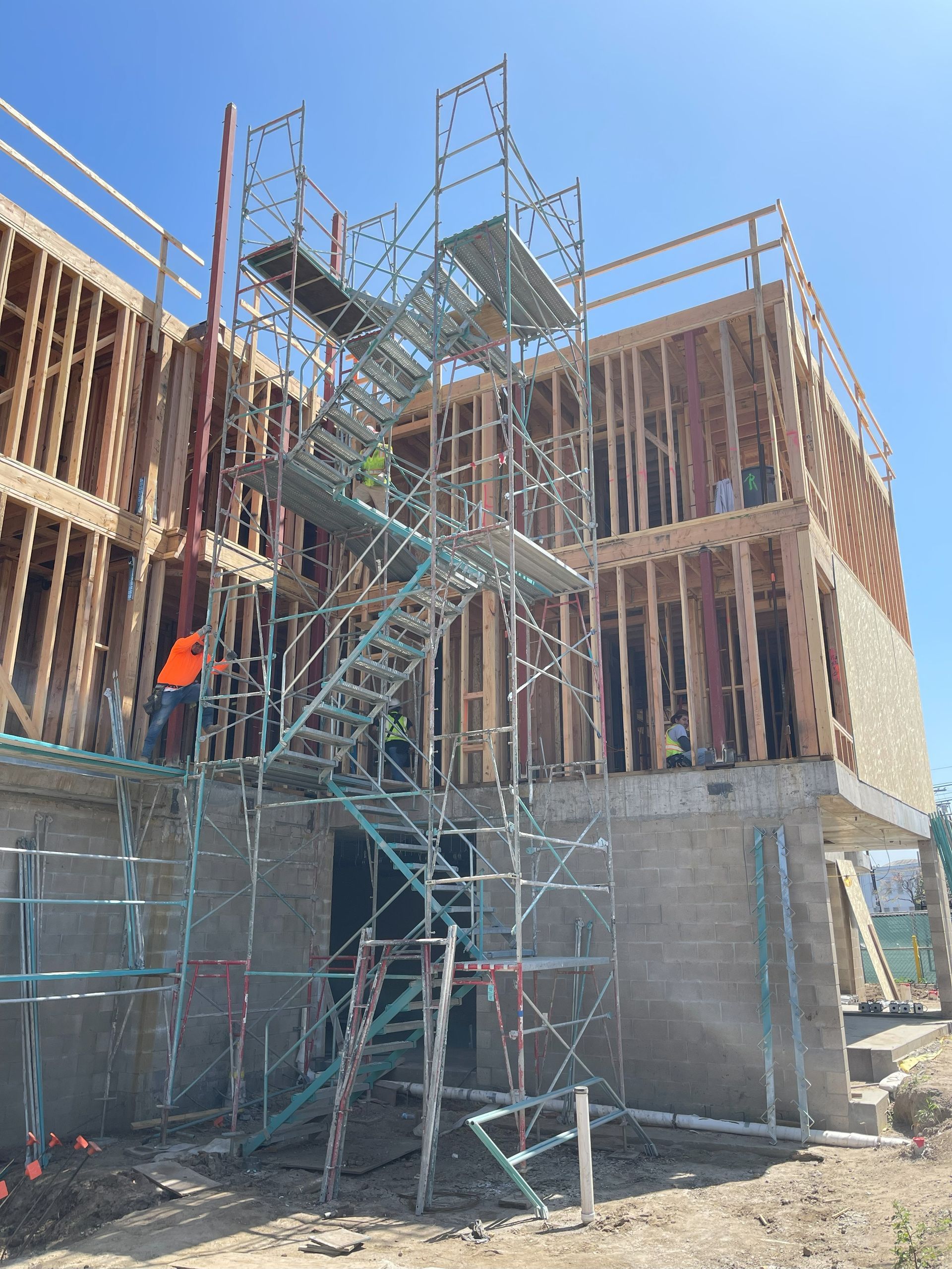 Construction site with multi-story wooden framed building and scaffolding on a sunny day.